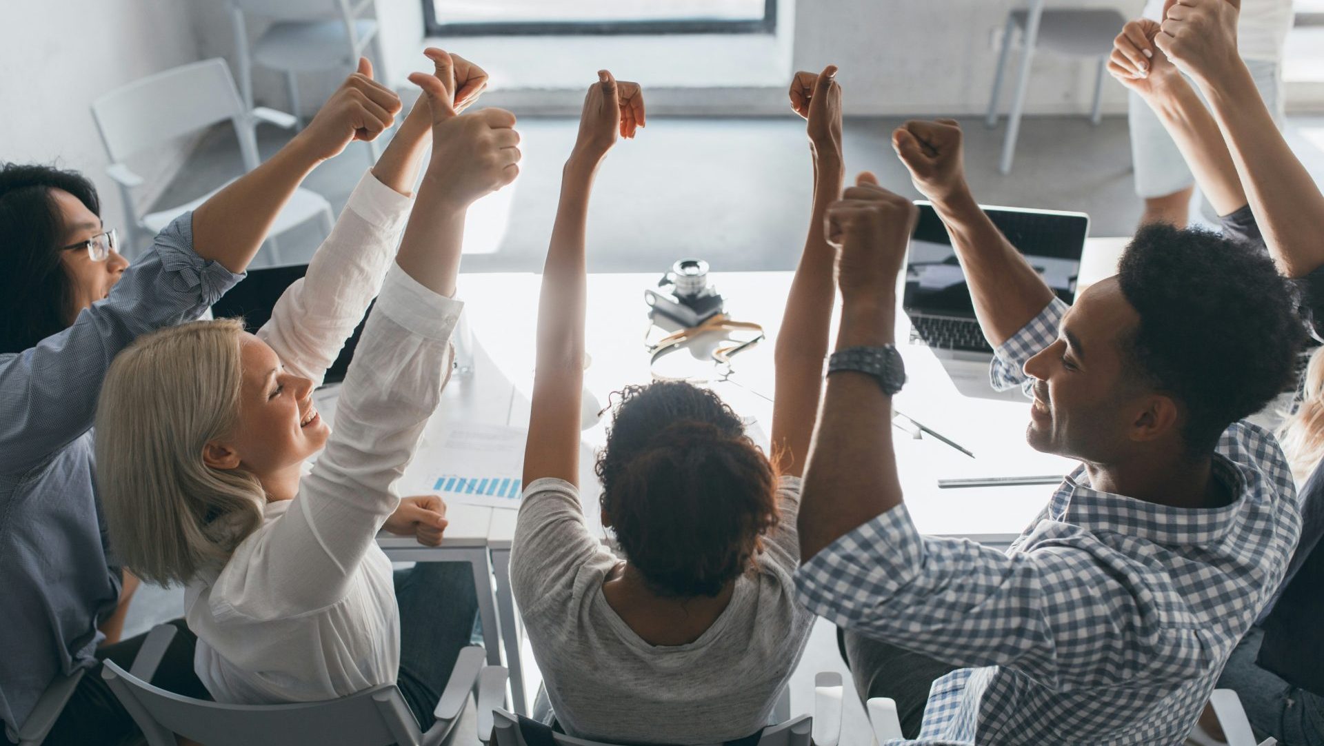 a group of people sitting at a table raising their hands